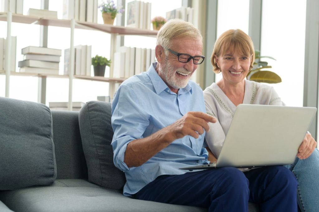 Un couple de personnes âgées est assis sur un canapé et rit en regardant l'écran d'un ordinateur portable