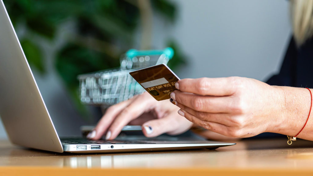 zoom sur une main de femme tenant une carte de crédit, et faisant un achat en ligne sur son ordinateur