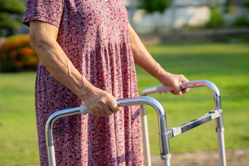 Une femme âgée s'appuie sur un cadre de marche pour se déplacer à l'extérieur