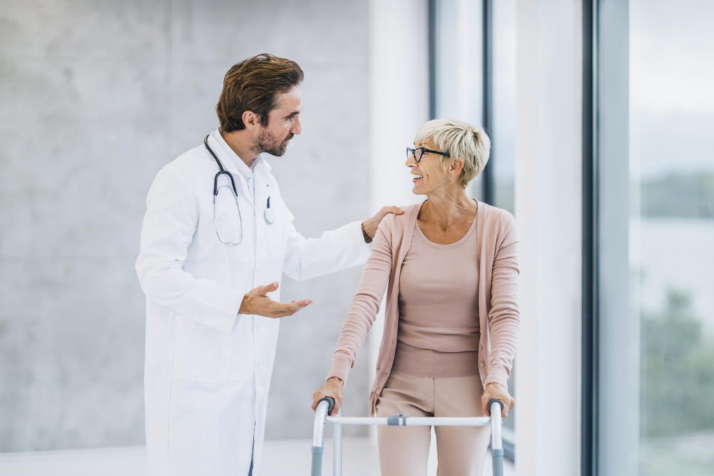 un docteur en blouse blanche discute avec une femme âgée utilisant un cadre de marche