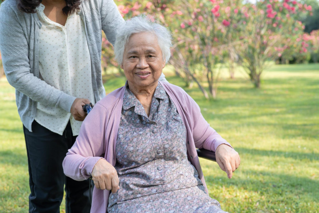 femme âgée assise sur un fauteuil roulant, avec une aide derrière elle